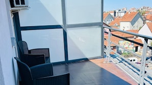 Een balkon met uitzicht op de stad, een zwarte rieten stoel en een witte airconditioning.