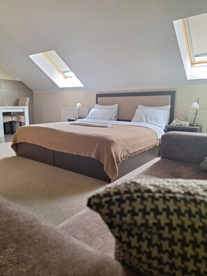 A modern hotel room with a large bed, a desk, and two chairs. There are skylights above the bed. - Hotel Ema (Kragujevac)