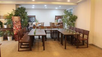 Un salón de conferencias con largas mesas y sillas, plantas en macetas y un cartel que anuncia servicios de catering.