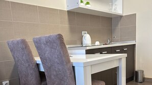 Een kleine keuken met een wit aanrecht, twee stoelen, een spoelbak en een spiegel boven het aanrecht.