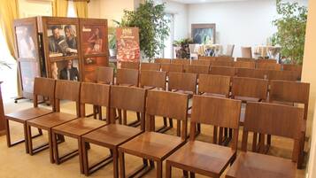 A conference room with rows of wooden chairs and tables, a podium with a poster, and potted plants.
