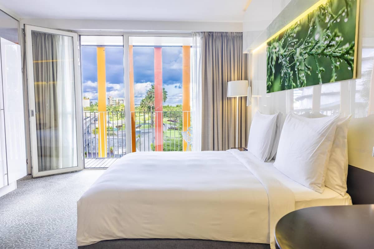 A hotel room with a large bed, a view of the outside, and a sliding glass door.