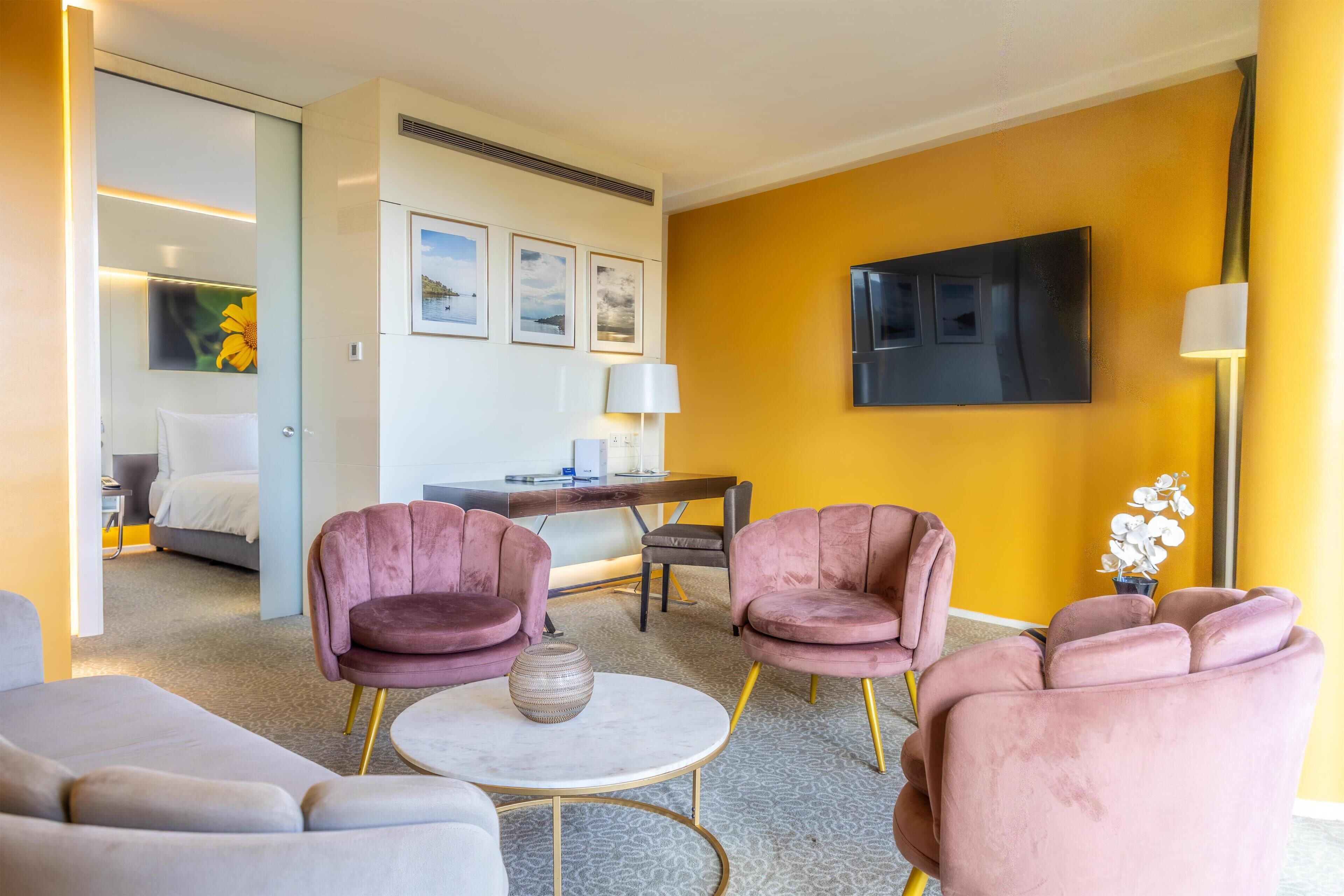 Een moderne woonkamer met een bank, twee fauteuils, een salontafel en een flatscreen televisie aan de muur.