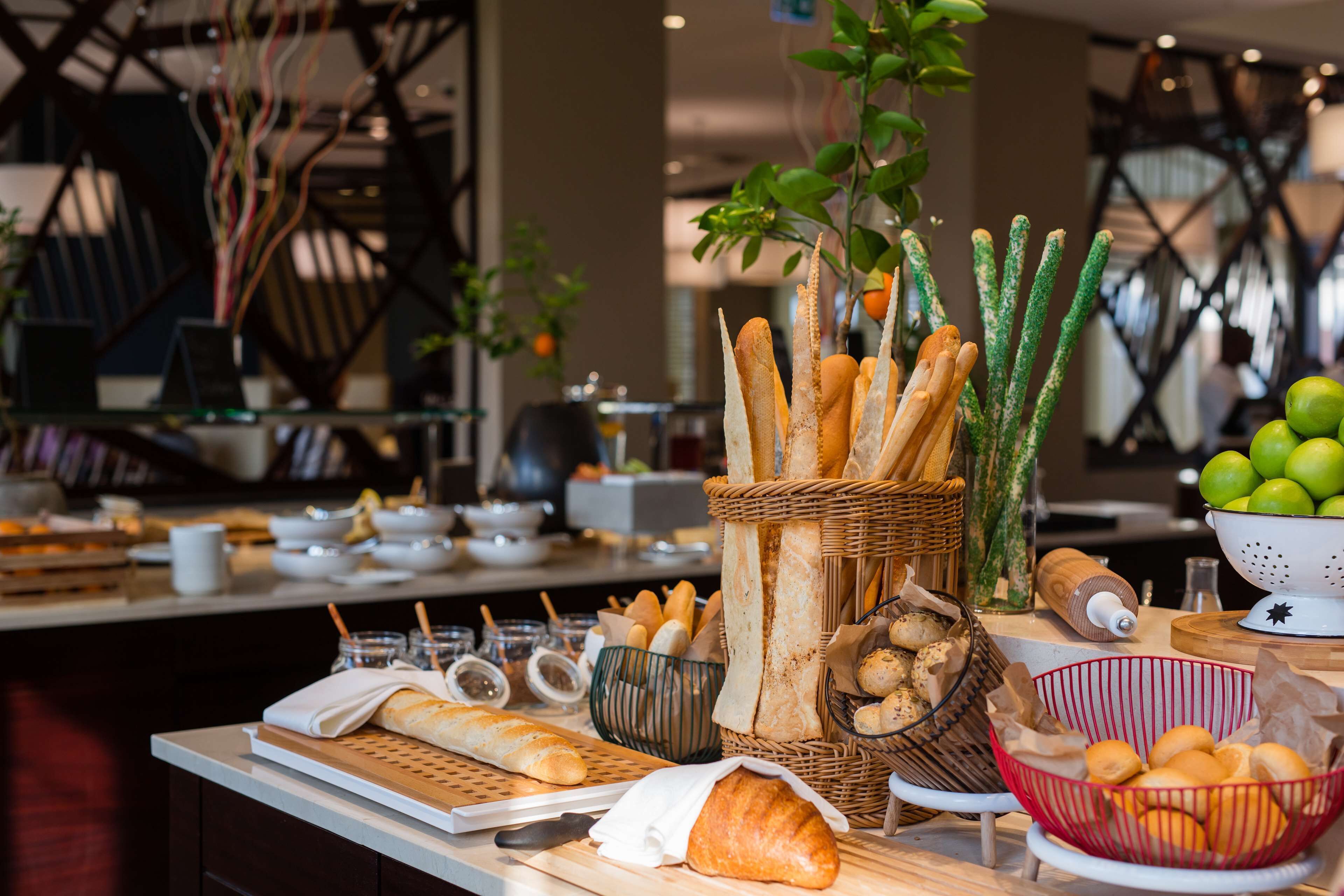 A buffet table with various breads, a basket of baguettes, a bowl of oranges, and a basket of mushrooms.