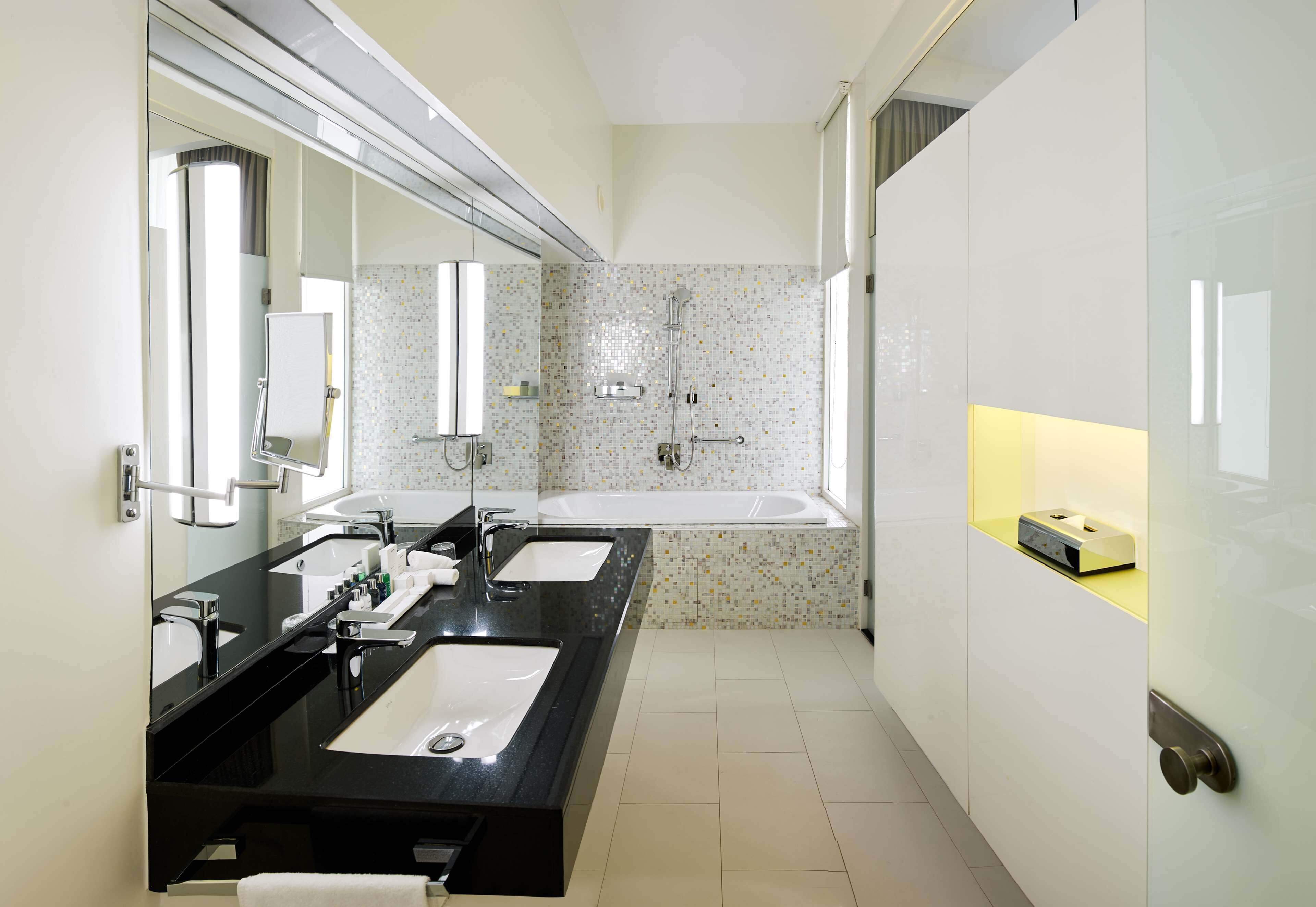 Ein modernes Badezimmer mit zwei Waschbecken, einem großen Spiegel, einer Badewanne und einem Waschtisch mit Seifenspender.