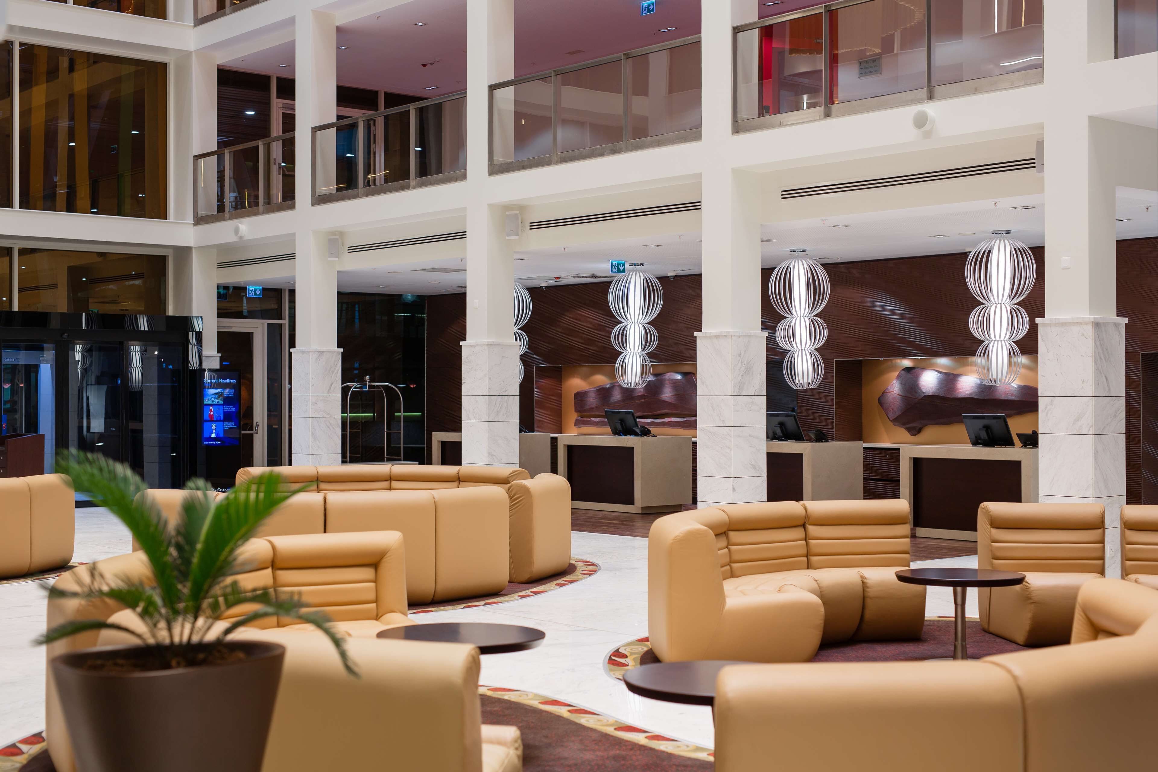 A spacious lobby with multiple seating areas, a reception desk, and a large potted plant.