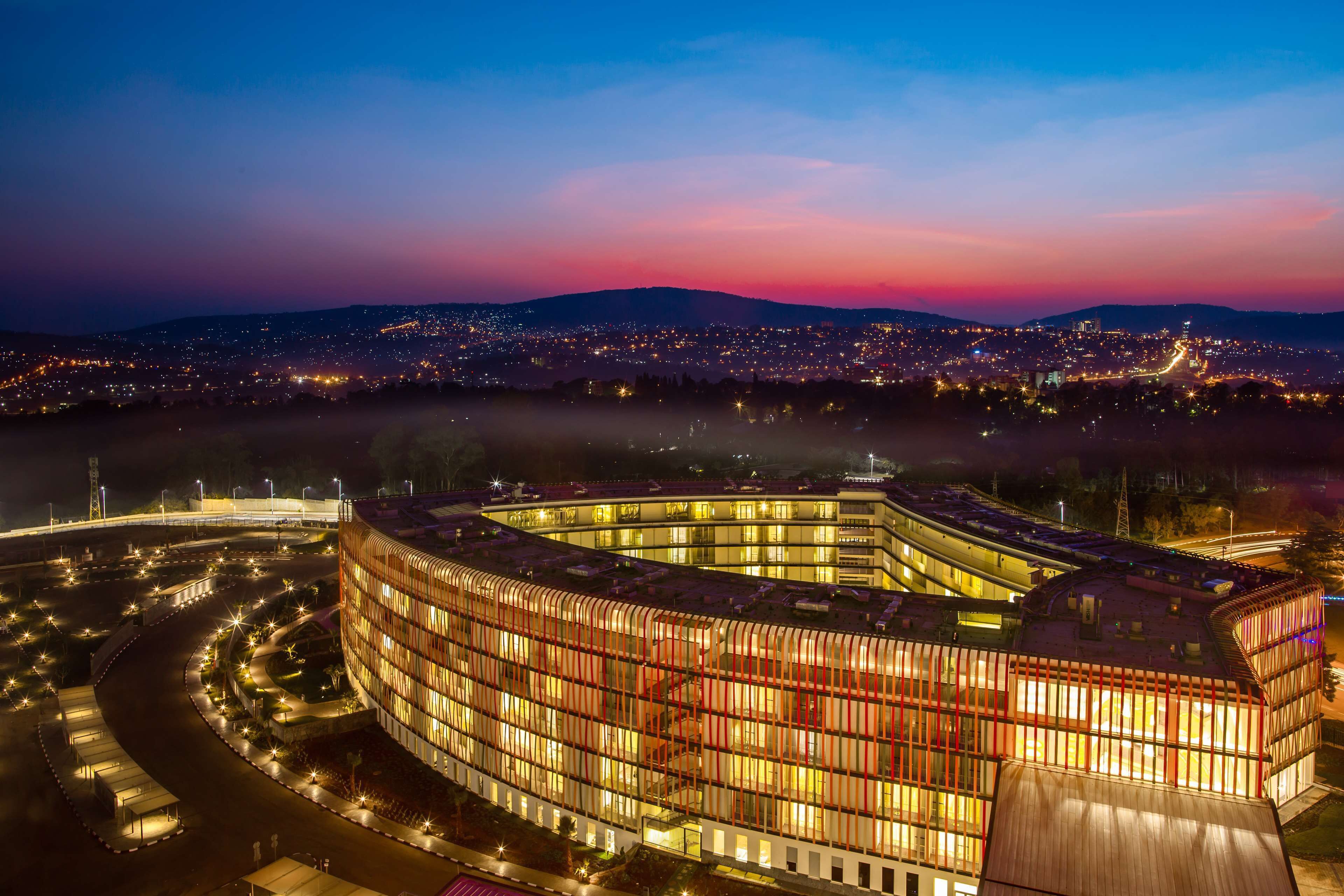 Un edificio moderno con facciata curvilinea, circondato da un'area di parcheggio ben illuminata e uno sfondo urbano.