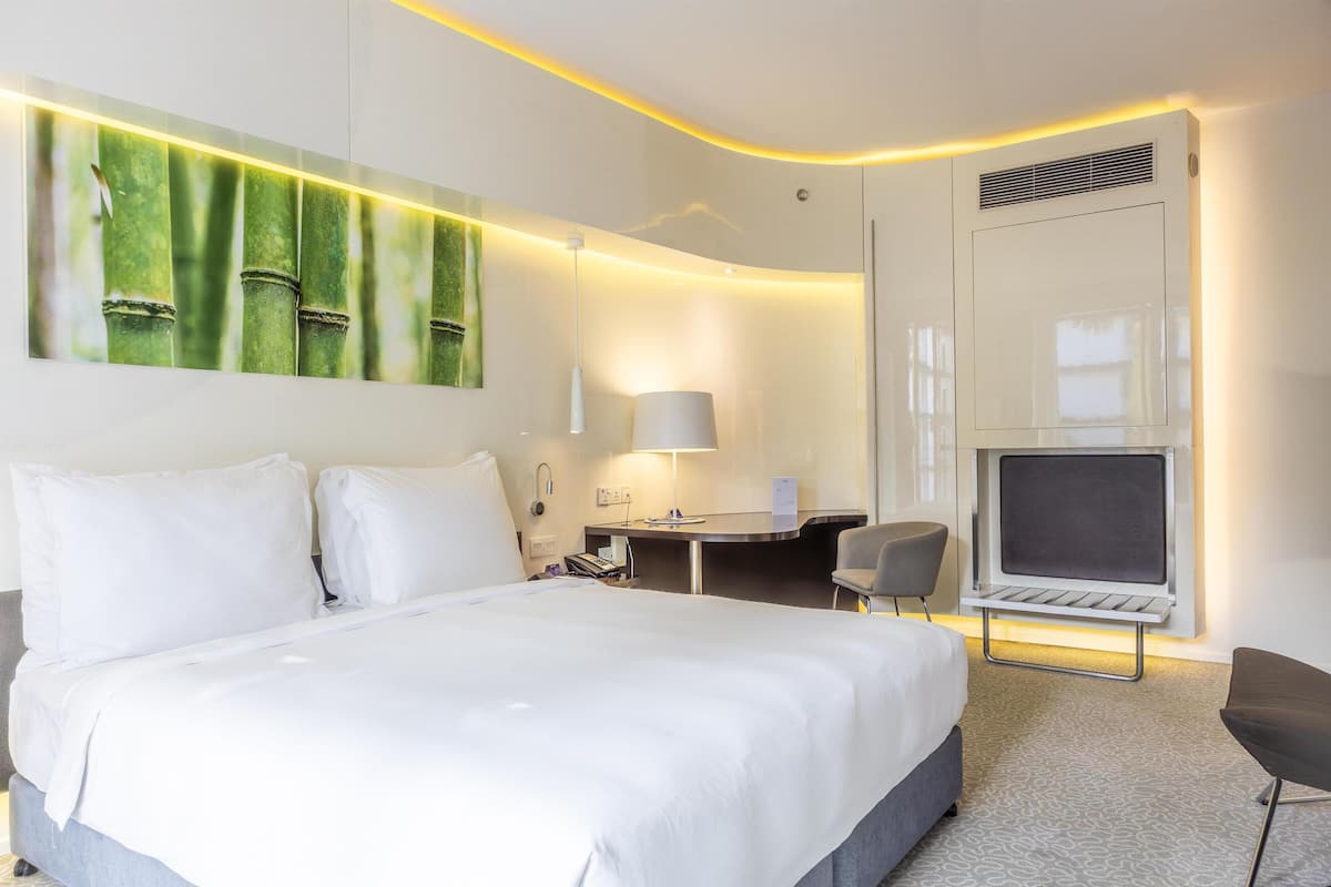 A modern hotel room with a large bed, a desk, a chair, and a TV.