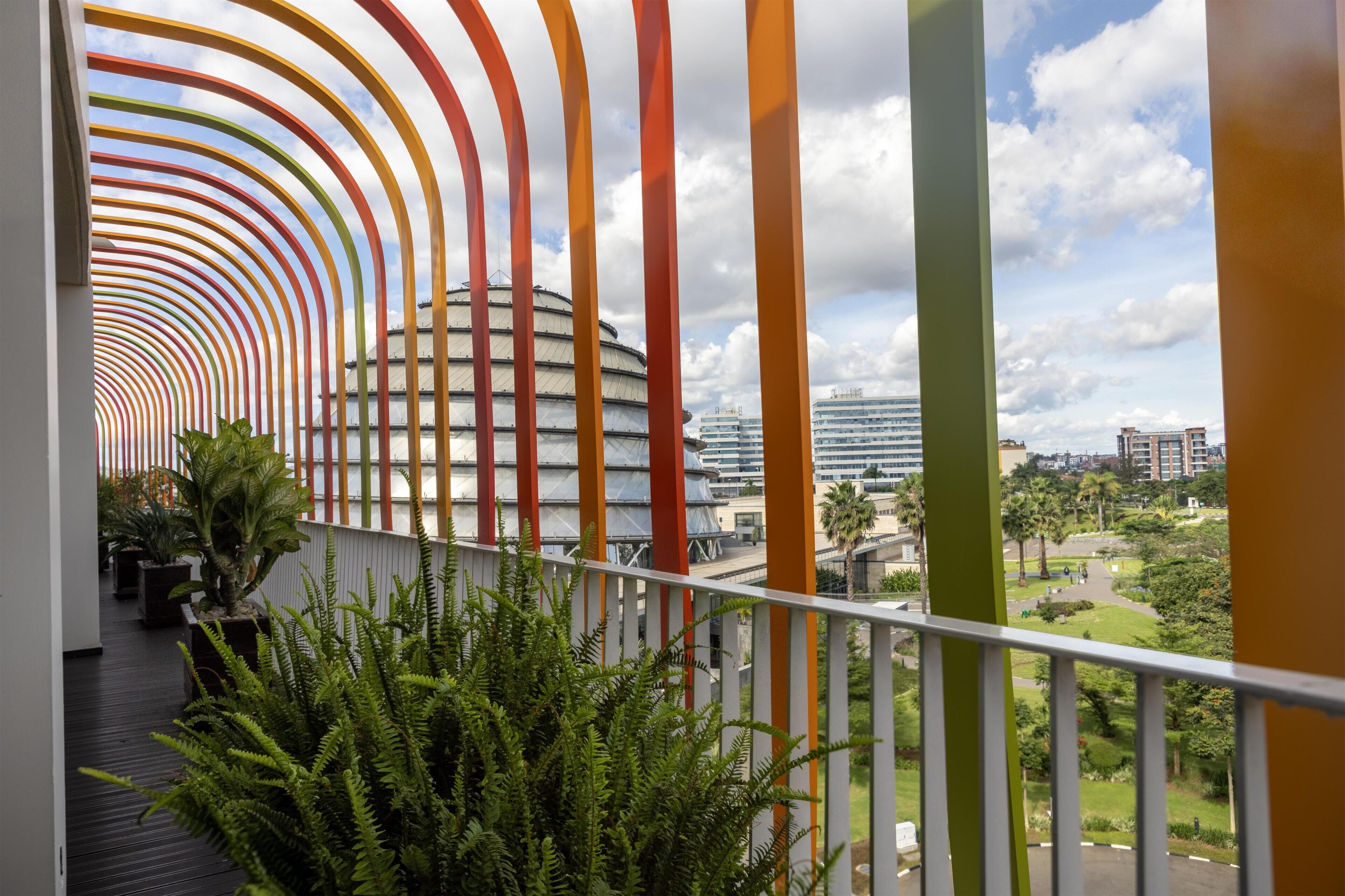 Un couloir doté d’une rambarde colorée et incurvée, offrant une vue sur un bâtiment moderne et sur la verdure environnante.