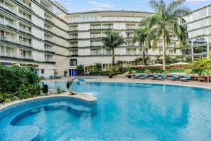 A hotel with a swimming pool surrounded by lounge chairs and palm trees. - Radisson Blu Hotel & Convention Centre, Kigali (Kigali)