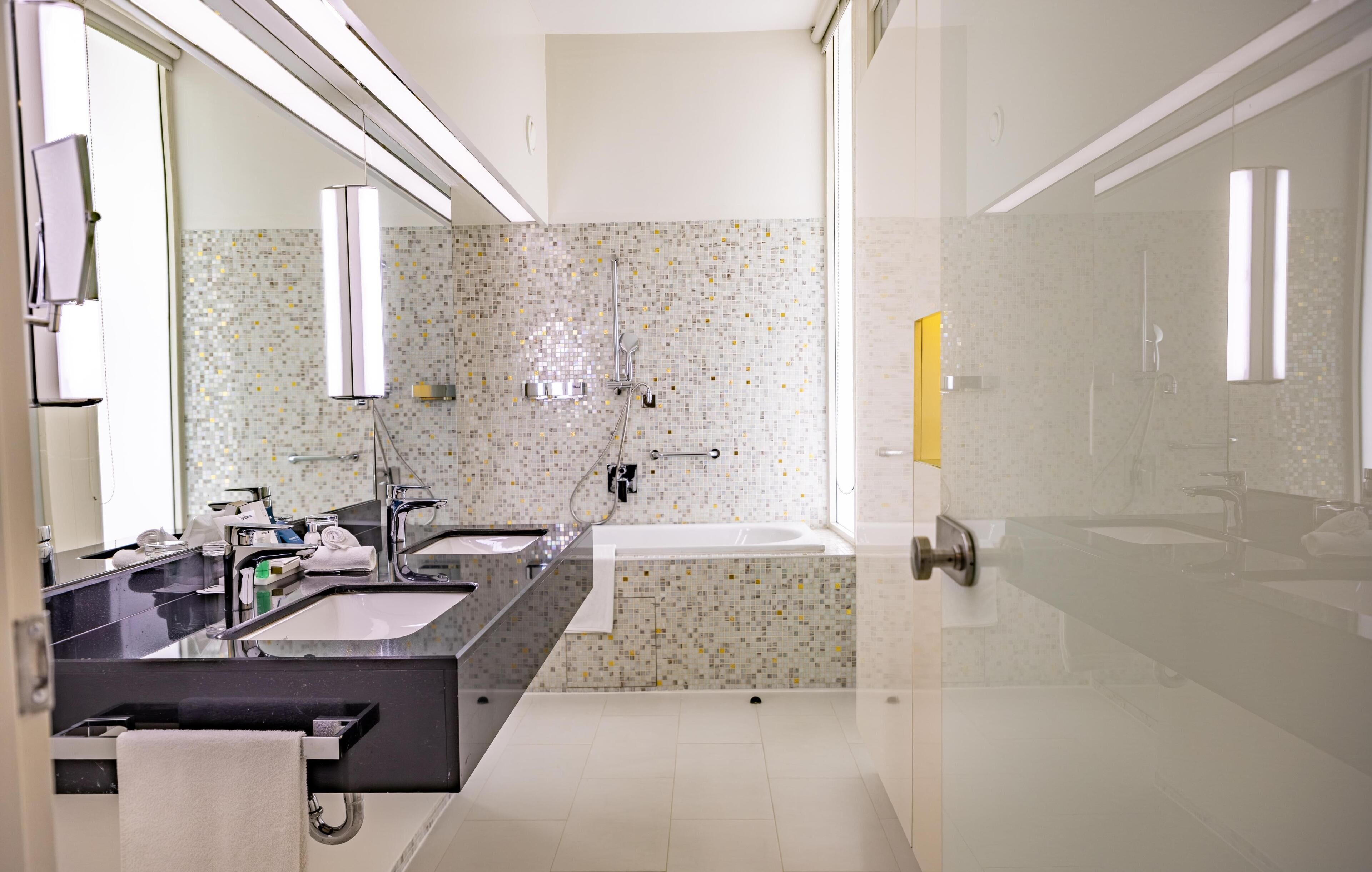 Een moderne badkamer met een grote spiegel, twee wastafels, een bad en een douche.