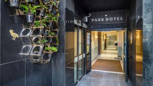 Une entrée d’hôtel moderne, avec un mur réfléchissant et une enseigne indiquant « Park Hotel ».