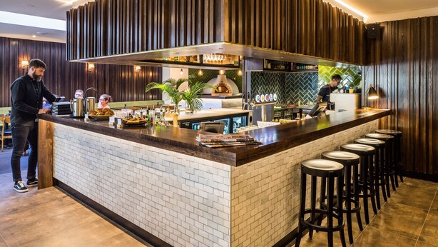 Uma área de bar moderna com balcão de tijolos, banquetes e forno a pizza.