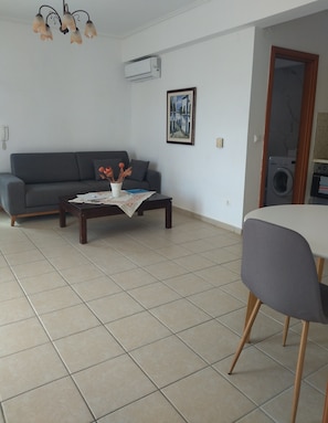Una sala de estar con un sofá, una mesa de centro con adornos, un comedor con mesa y sillas, y un equipo de aire acondicionado en la pared.