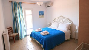 A bedroom with a bed, a chair, a window with curtains, a painting, and an air conditioning unit. - Lagoon View Apartments - Adults Only (Kefalonia)
