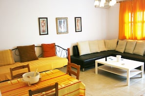 A living room with a sofa, a dining table with chairs, and a coffee table. There are three framed pictures on the wall.