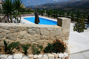 A stone wall with a pool and plants, overlooking a mountainous landscape.