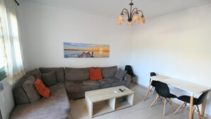 A living room with a sectional sofa, a coffee table, a dining table with chairs, and a painting on the wall. - Lagoon View Apartments - Adults Only (Kefalonia)