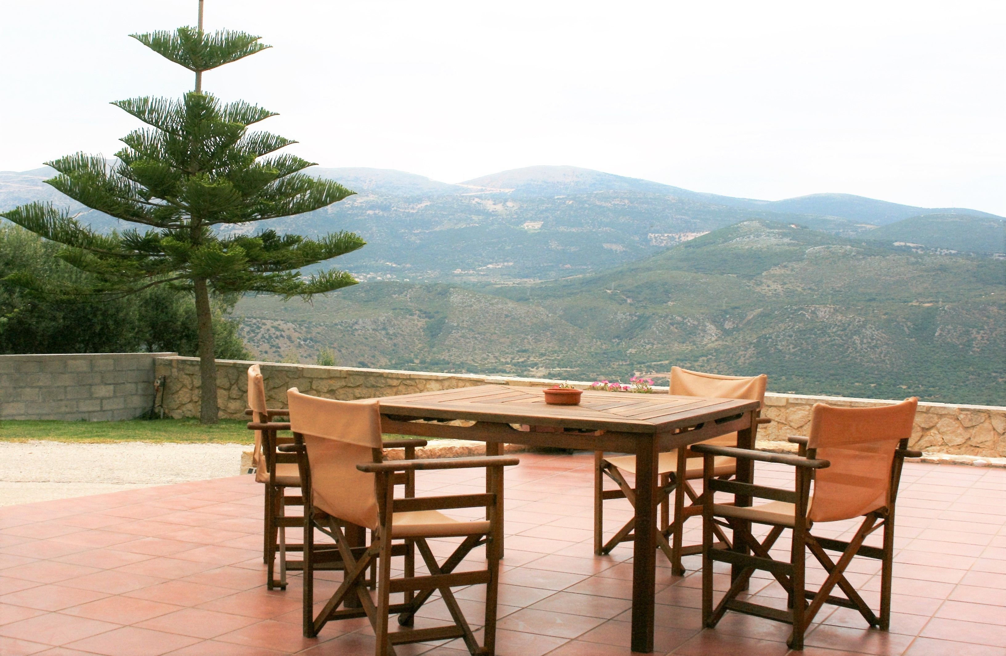 Ein Holztisch mit Stühlen auf einer Terrasse, mit Blick auf die Berge.
