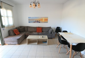 A living room with a sofa, a coffee table, a dining table with chairs, and a painting on the wall. - Lagoon View Apartments - Adults Only (Kefalonia)