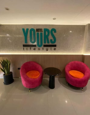 A reception area with a sign reading "YOURS lifestyle" and two pink chairs with orange cushions. - YOURS HOTEL LIFESTYLE (Chiclayo)
