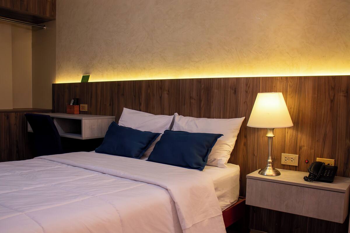 Ett hotellrum med en säng, ett nattduksbord, en lampa och ett skrivbord med en stol.