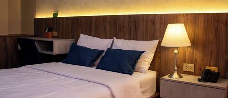 A hotel room with a bed, bedside table, lamp, and a desk with a chair.