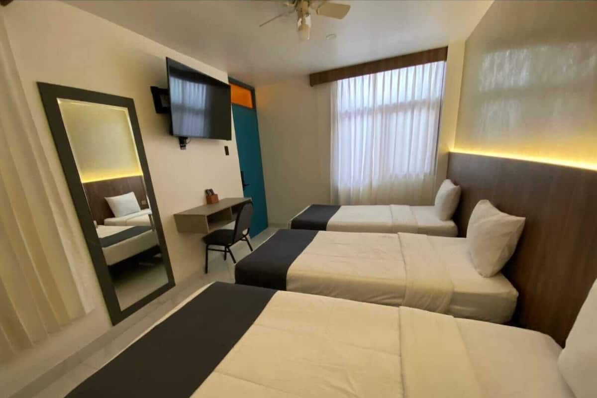 Ett hotellrum med två sängar, ett skrivbord, en stol, en TV som är monterad på väggen och ett fönster med gardiner.