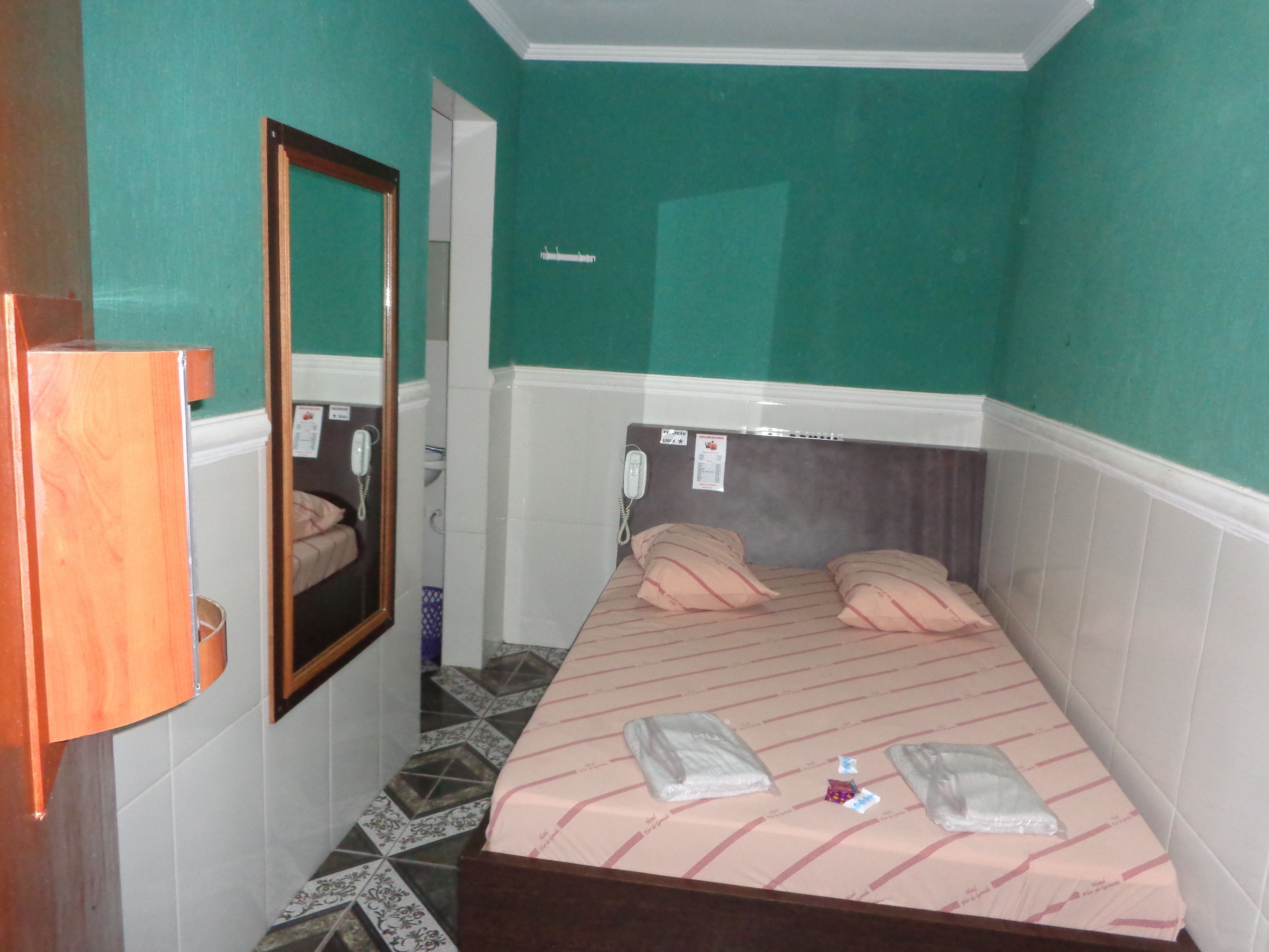 A small, narrow room with a bed, a mirror, and a telephone.