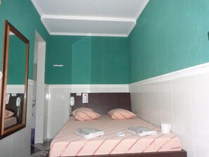 A hotel room with teal walls, a bed with pink bedding, a mirror, and a bedside table with a cup. - Hotel Flor do Gomide (São Paulo)
