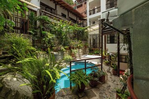 Une cour avec une piscine, entourée de plantes en pot et d’un mur de pierre.