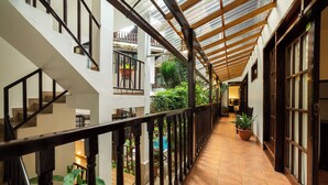 A covered corridor with a wooden railing, potted plants, and a view of a pool and greenery outside. - Gringo Bill's Boutique Hotel (Machu Picchu)