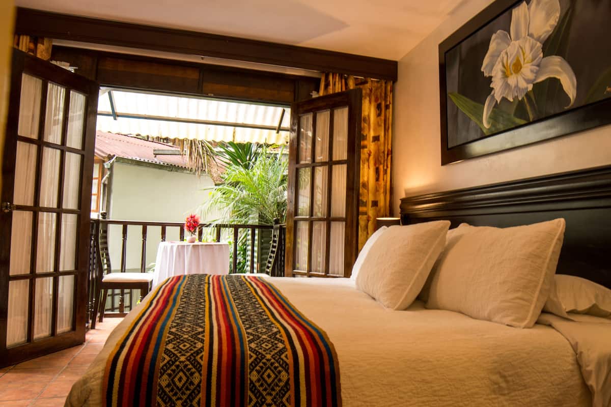 A hotel room with a bed, a nightstand, a framed picture of a flower, and a balcony with a table and chairs.