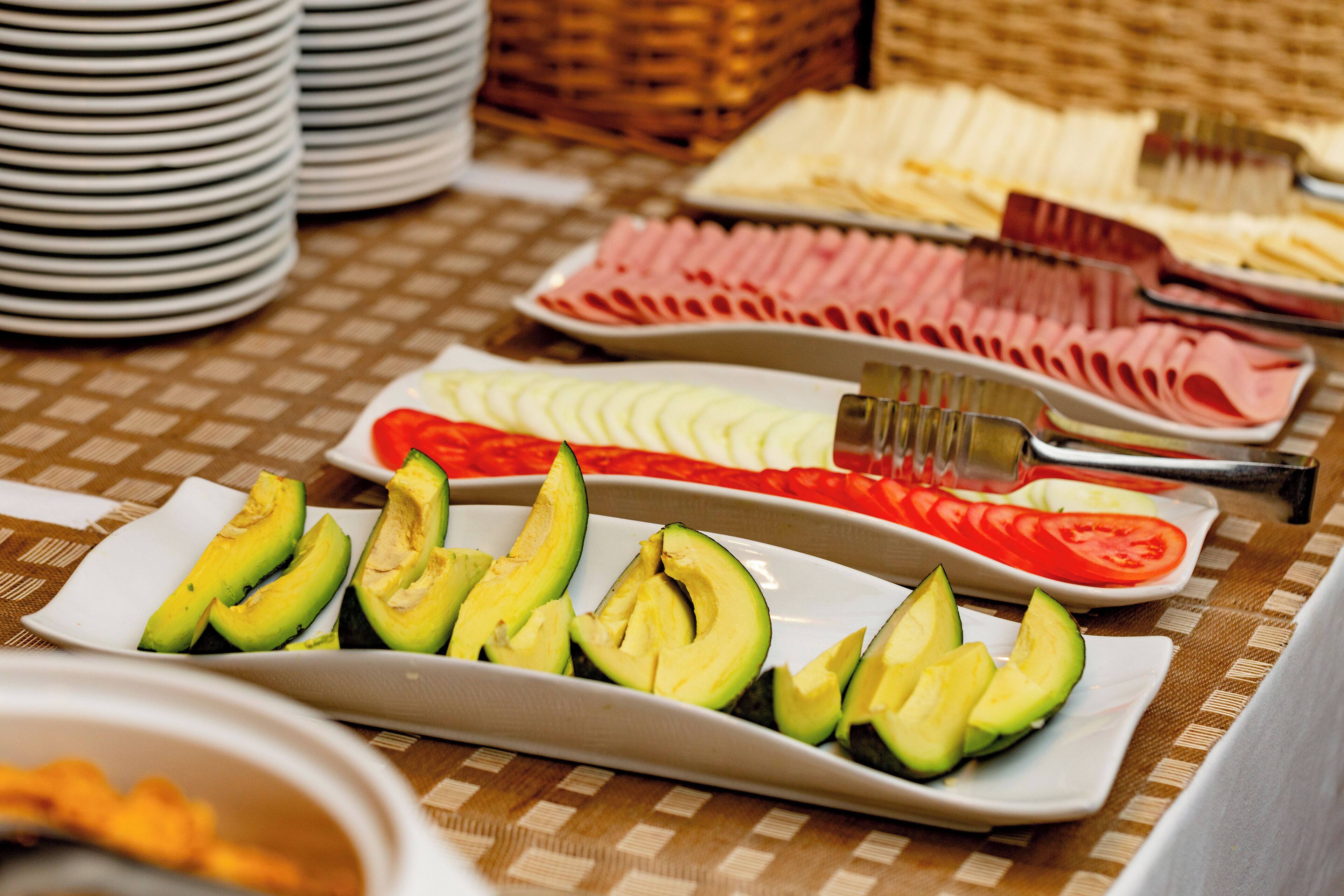 A buffet table with various food items including sliced avocados, tomatoes, and different types of cheese.