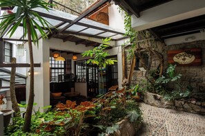 Un interior acogedor y rústico con pared de piedra, vigas de madera y abundante verdor.