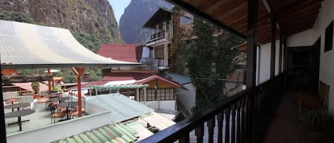 A balcony with a view of a mountainous landscape, a covered outdoor seating area, and a building with multiple levels and balconies.