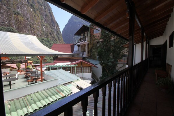 Un balcón con vistas a un paisaje montañoso, una zona de estar al aire libre techada y un edificio con varios niveles y balcones.
