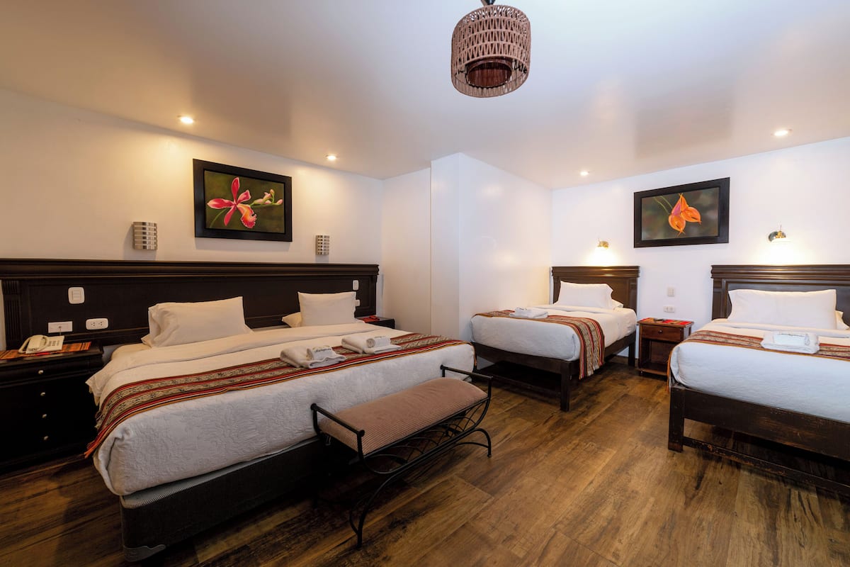 A hotel room with three beds, a bench, and a chandelier.