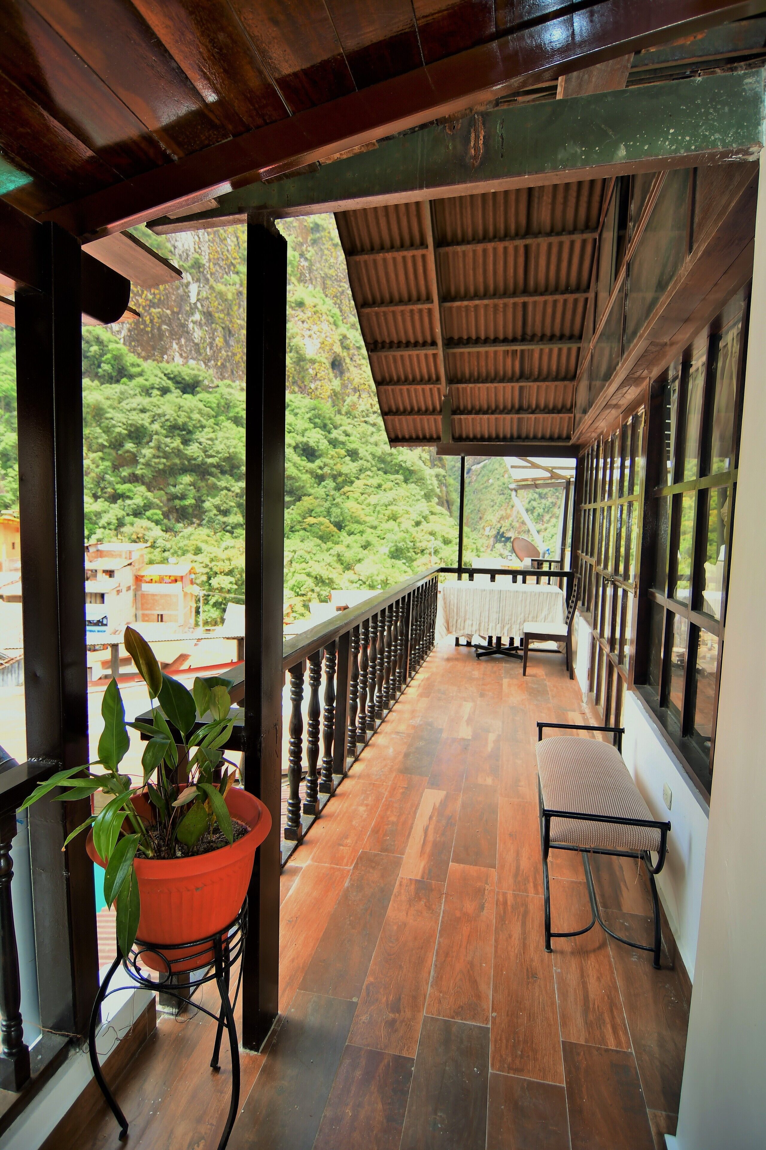 A wooden balcony with a tiled floor, a potted plant, and a table with chairs.