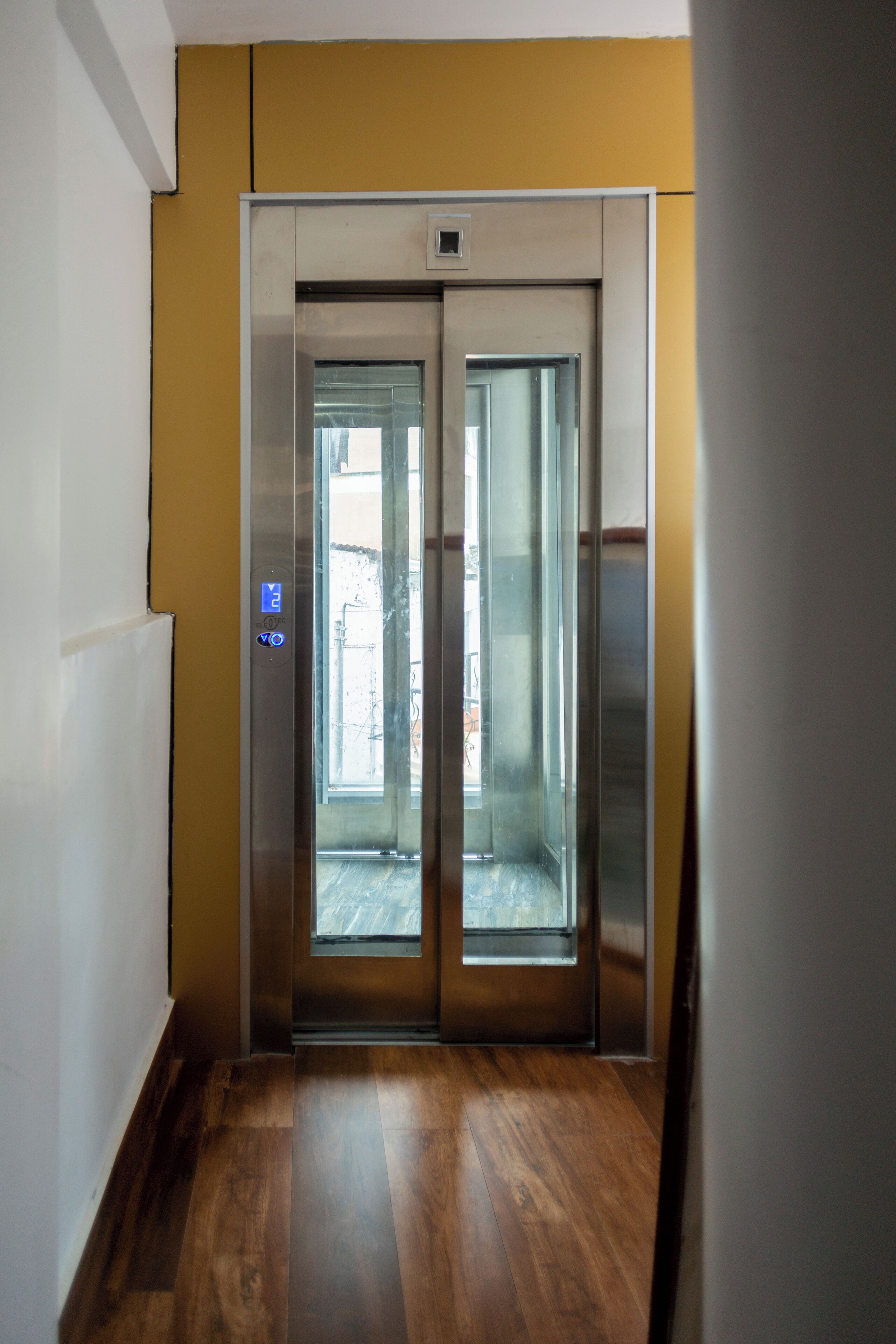 A hallway leading to an elevator with a yellow wall and wooden flooring.