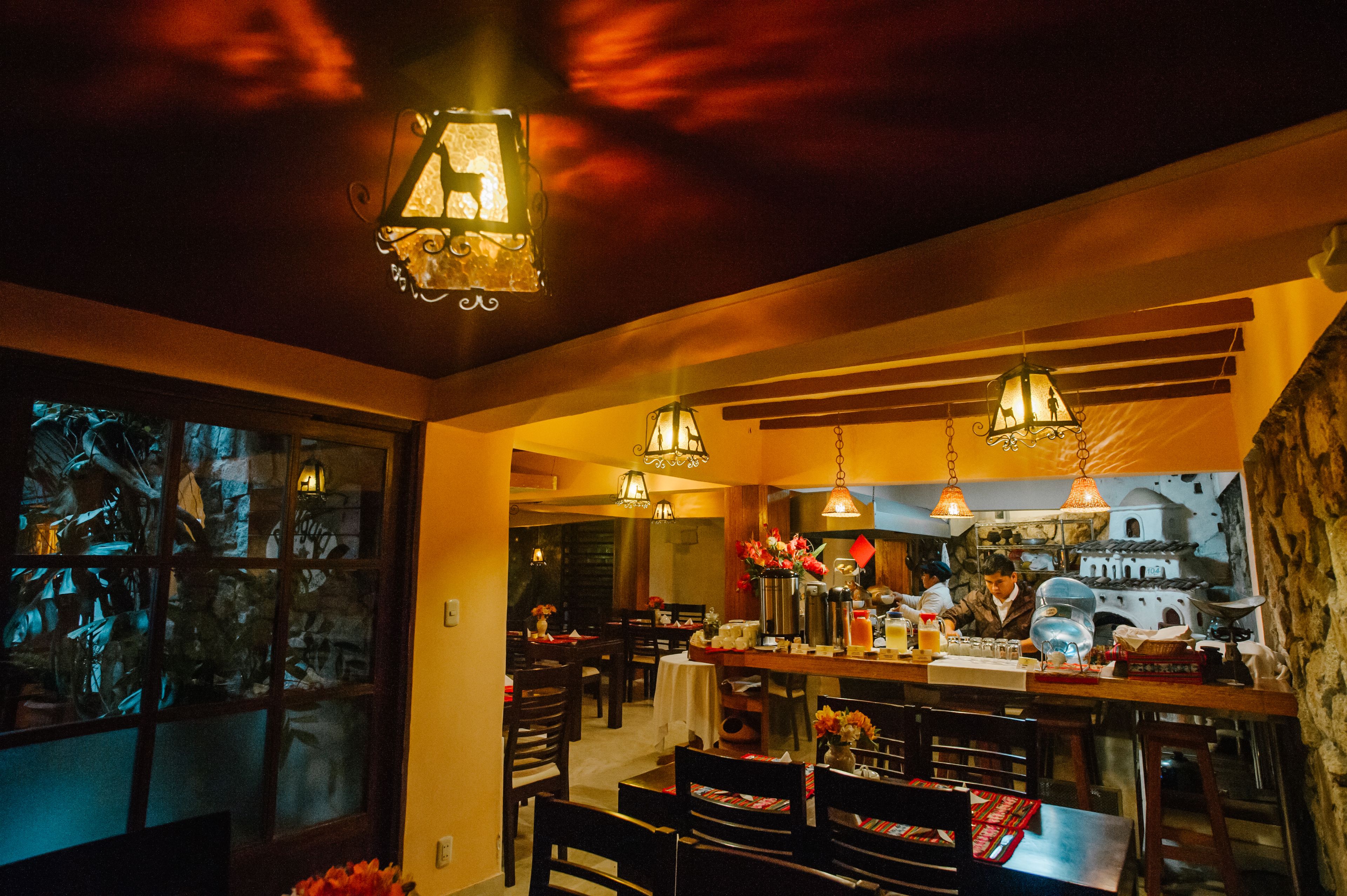A restaurant with wooden tables and chairs, hanging pendant lights, and a view of a building through a window.