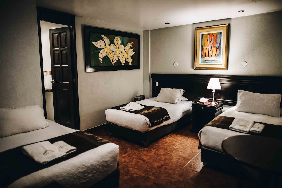 A hotel room with two single beds, a sitting area, a nightstand, and artwork on the walls.