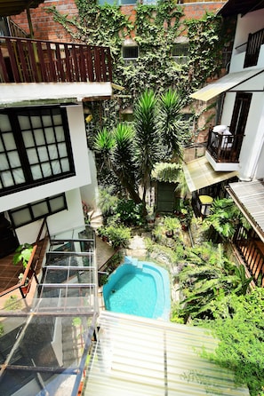 A residential courtyard with a swimming pool, lush greenery, and a multi-story building with balconies.