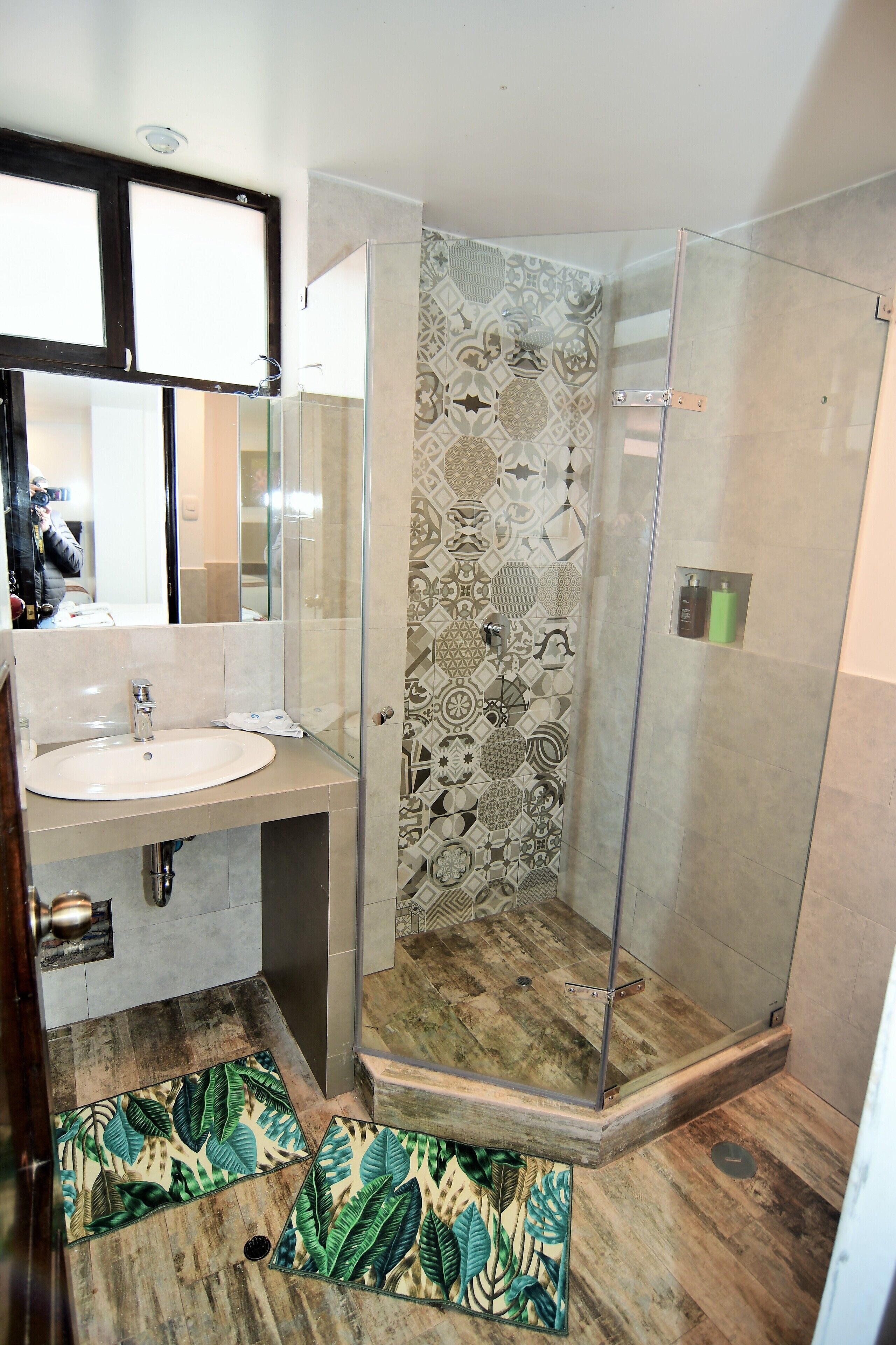 A bathroom with a glass shower enclosure, a sink, and patterned tiles.