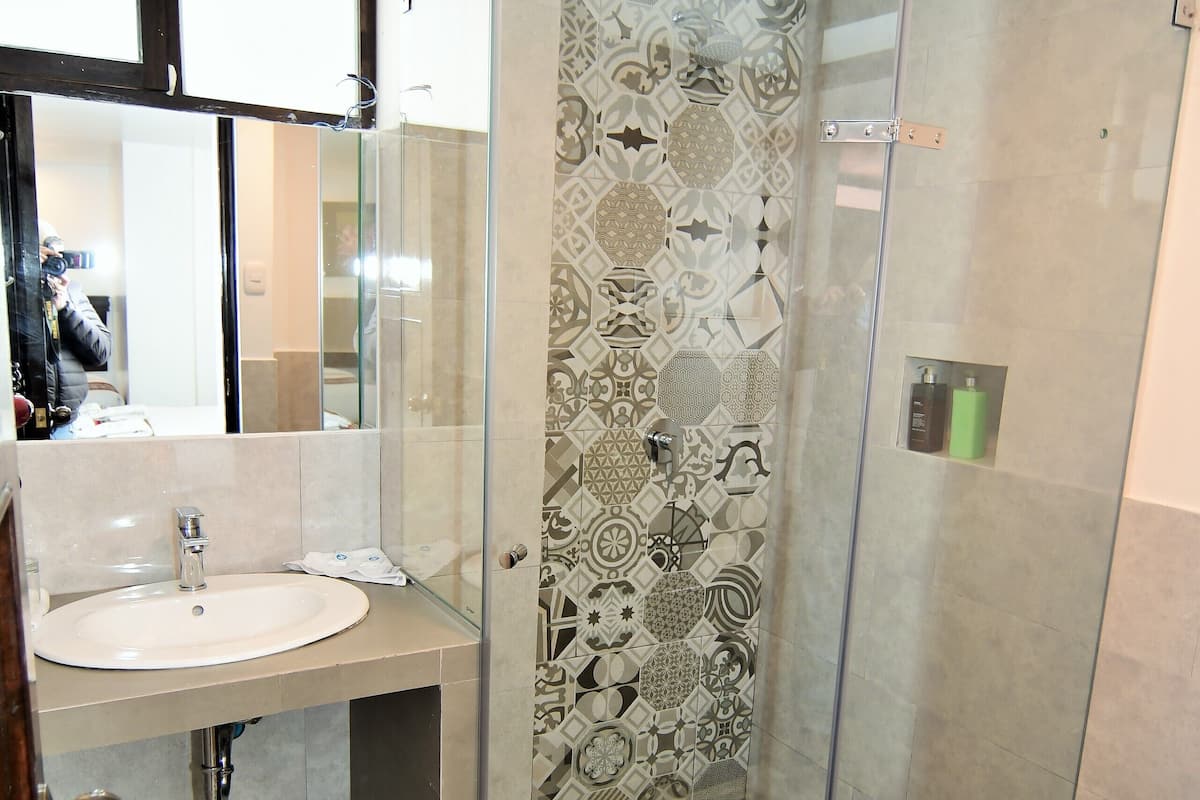 A bathroom with a glass shower enclosure, a sink, and patterned tiles.