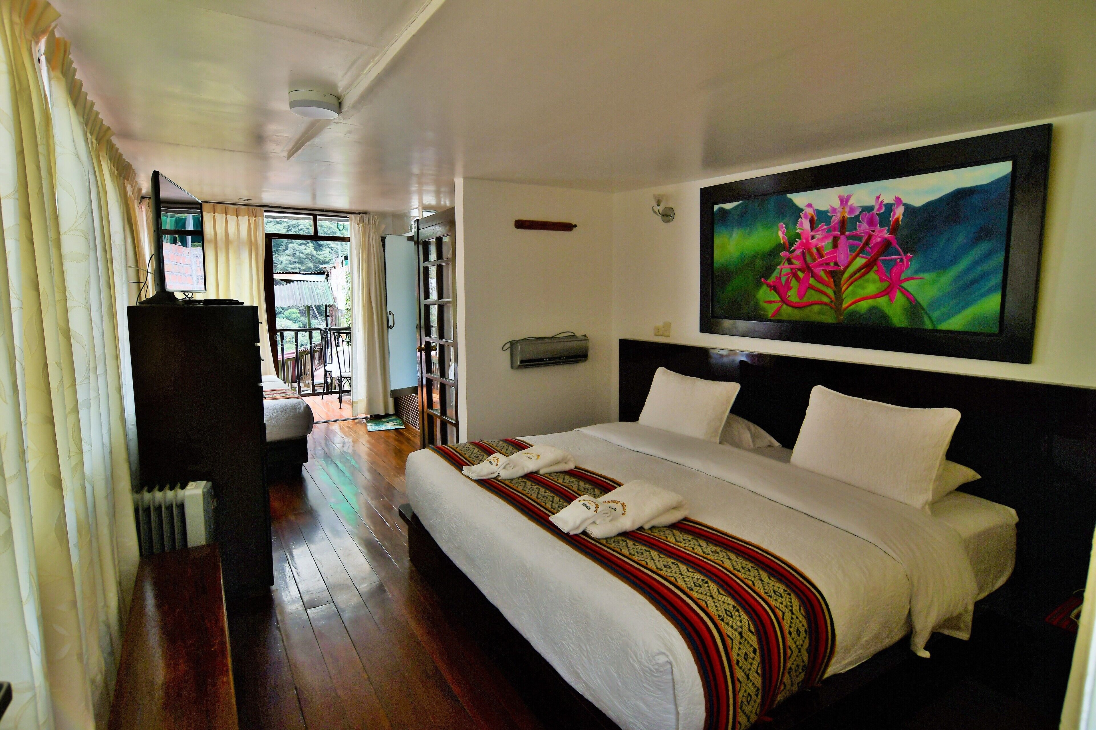 A hotel room with a large bed, a television, and a painting of flowers on the wall.