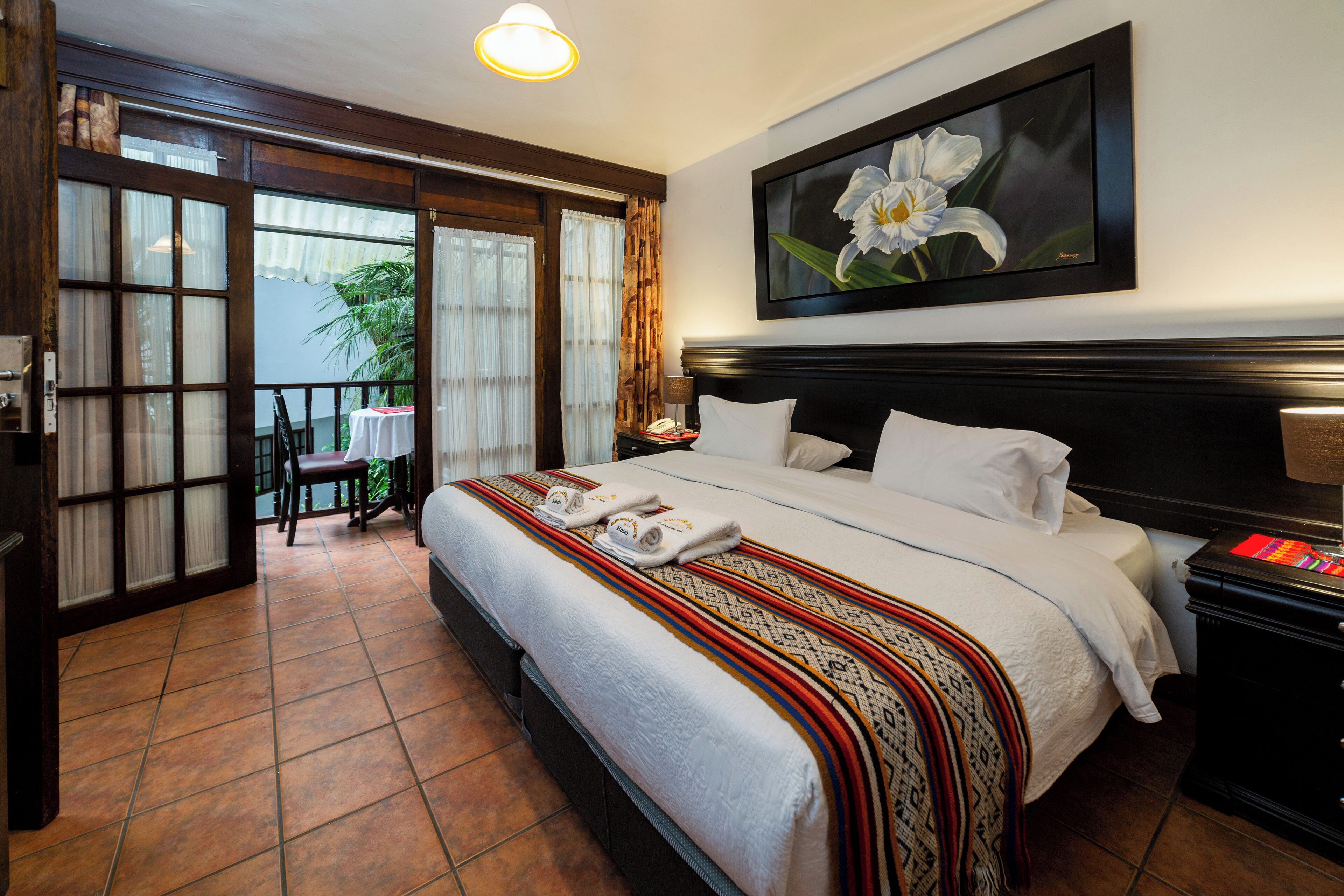 Habitación de hotel con una cama grande, un cuadro de una flor en la pared y vistas al balcón exterior.