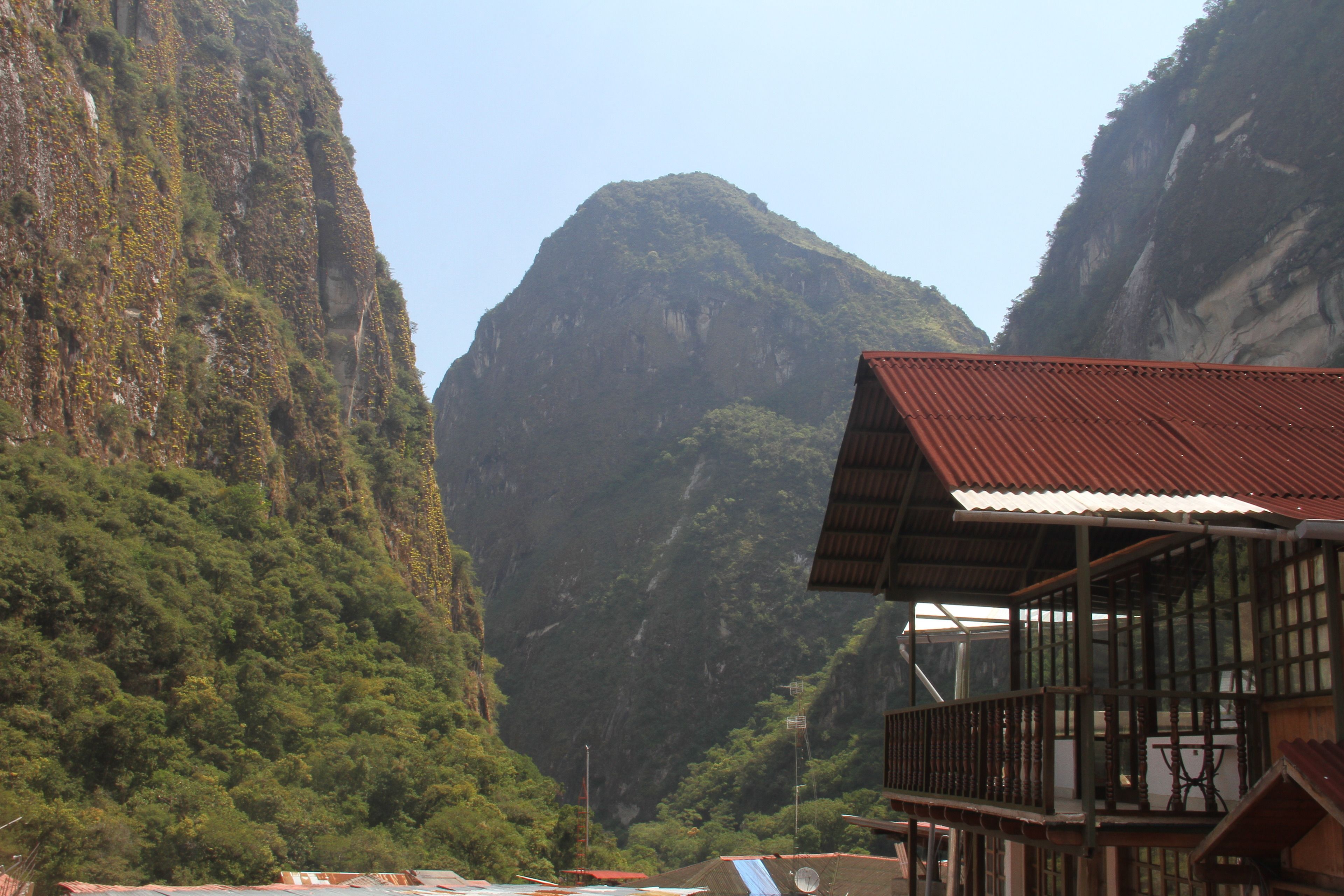A wooden building with a red roof, situated in a mountainous area with lush greenery and steep cliffs.