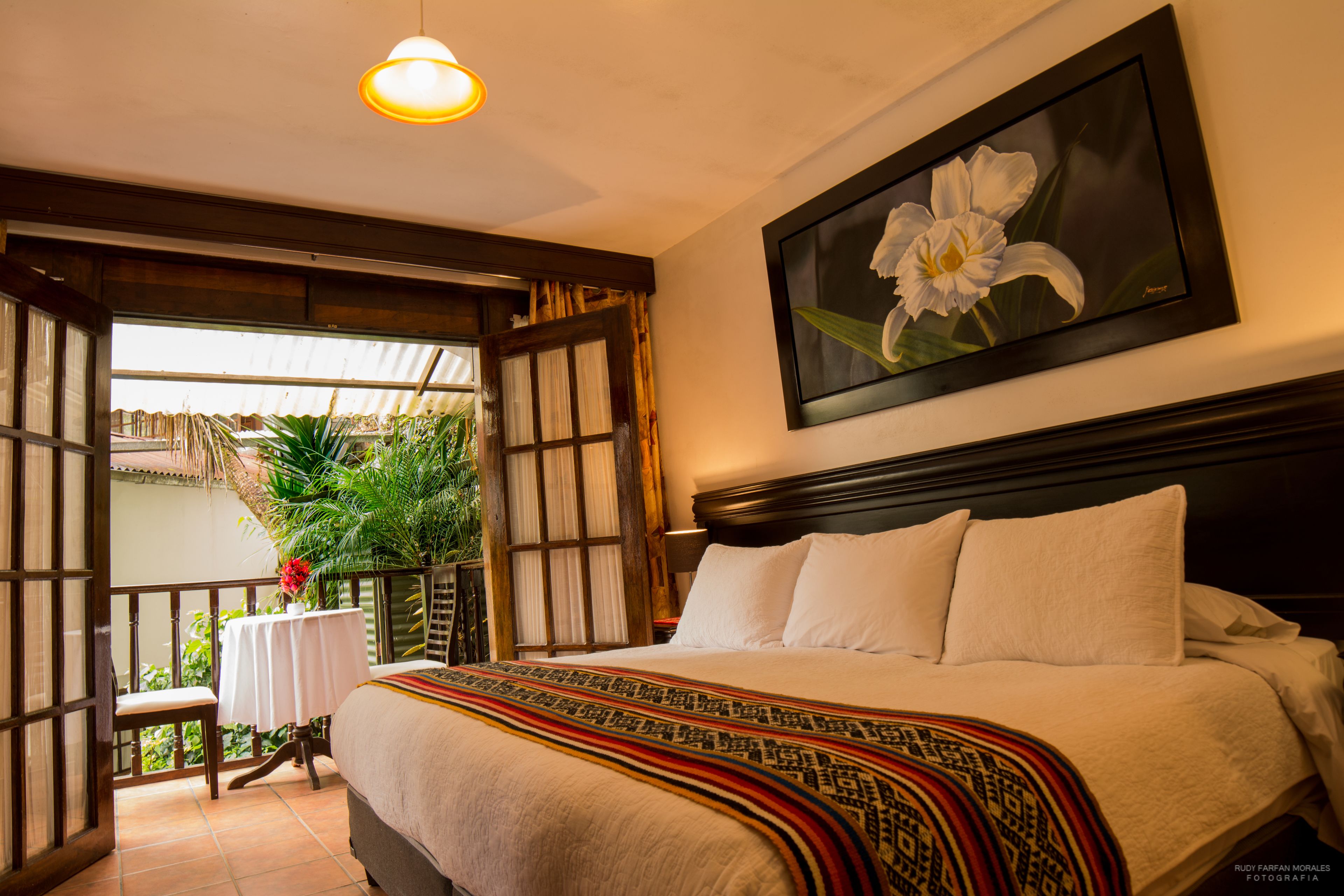 Een slaapkamer met een groot bed, een bloemschilderij aan de muur en een balkon met planten.