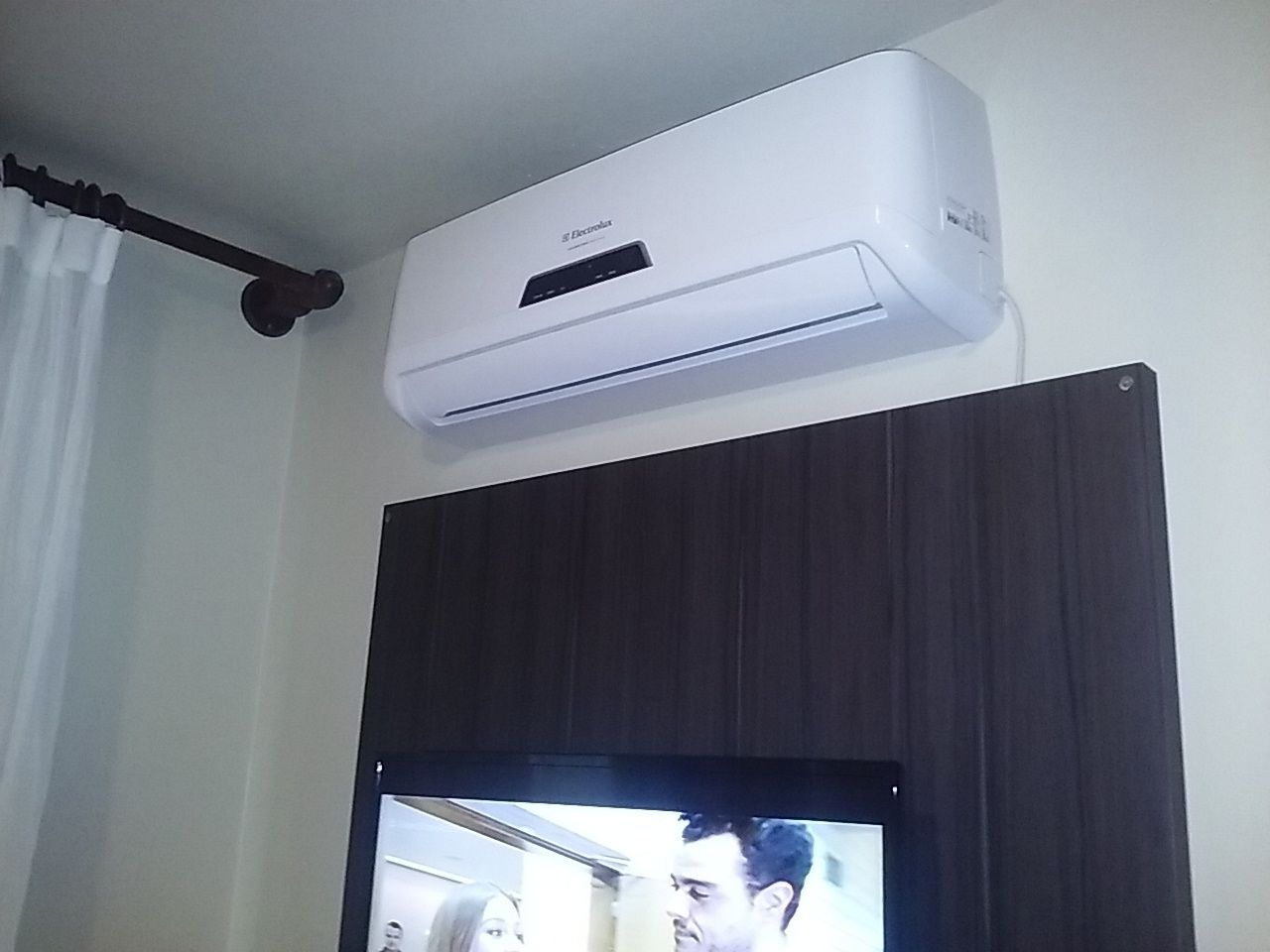 A room with a mounted air conditioner, a television, and a dark-colored cabinet.